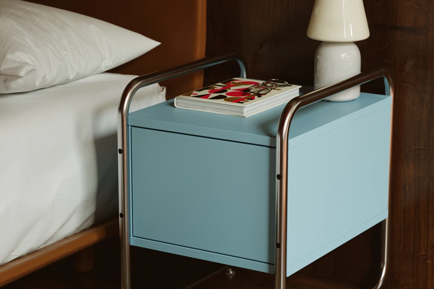 Szafka nocna Balt w błękitnym kolorze obok łóżka w pokoju hotelowym